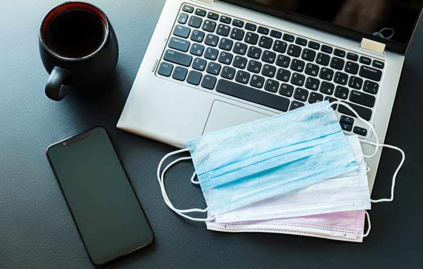 Medical masks on a laptop with a smartphone, antibacterial wipes and a cup of coffee on a black background.