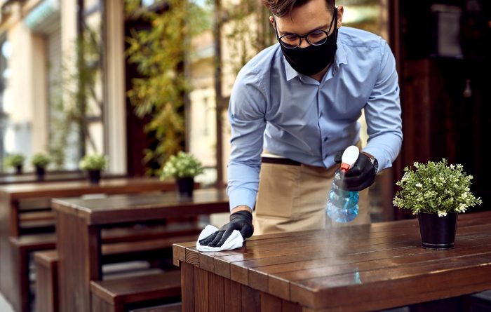 Waiter wearing protective face mask while disinfecting tables at outdoor