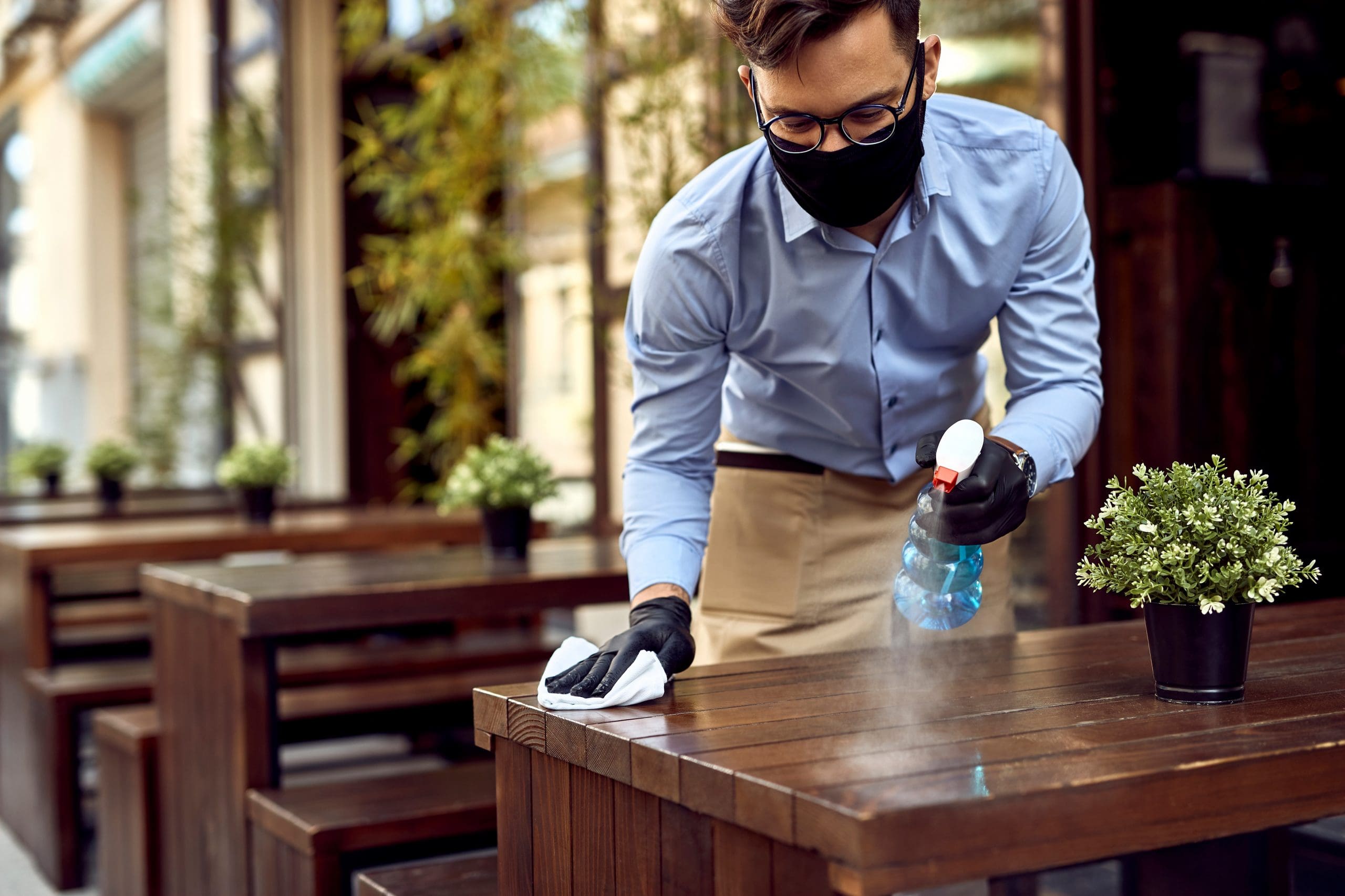 Waiter wearing protective face mask while disinfecting tables at outdoor