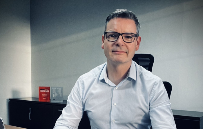 Andrew Hewitson, CEO of Reproflex3 sits at a desk in a blue shirt